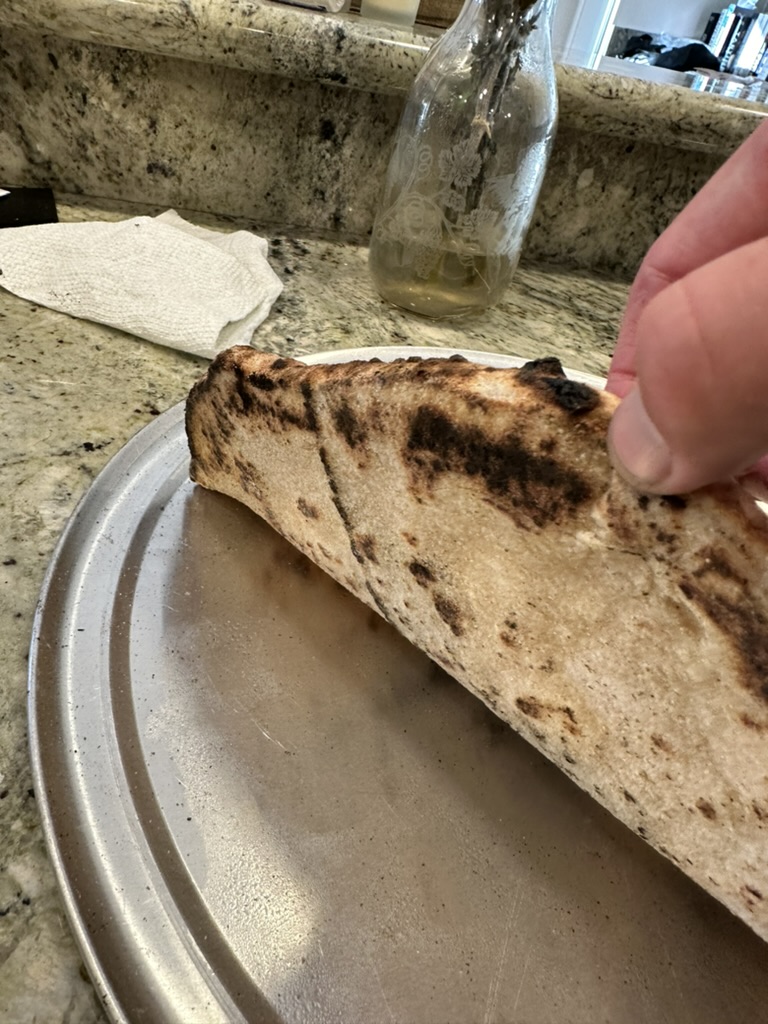 Charred underside of a pizza crust being lifted to show the bake