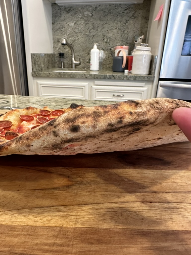 A pizza slice held upside down showing the charred and airy undercarriage