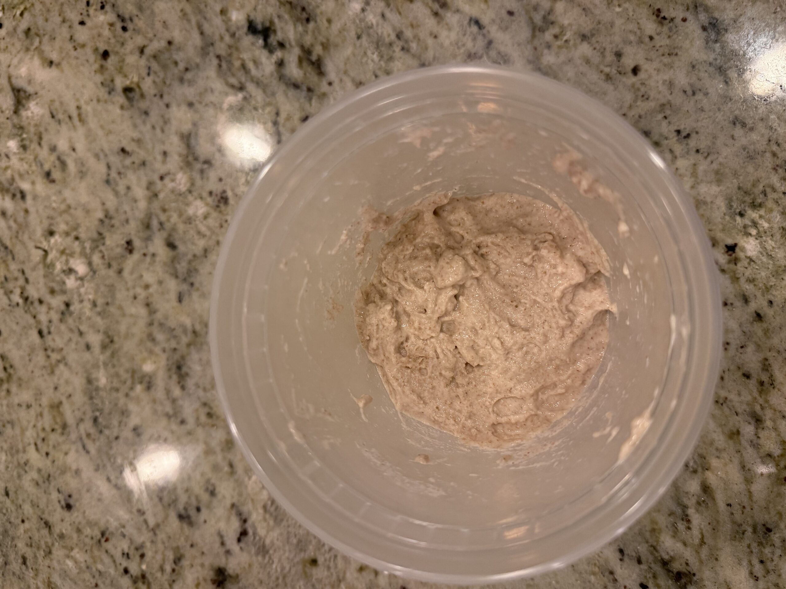 Freshly mixed poolish — a small amount of shaggy dough at the bottom of a clear container