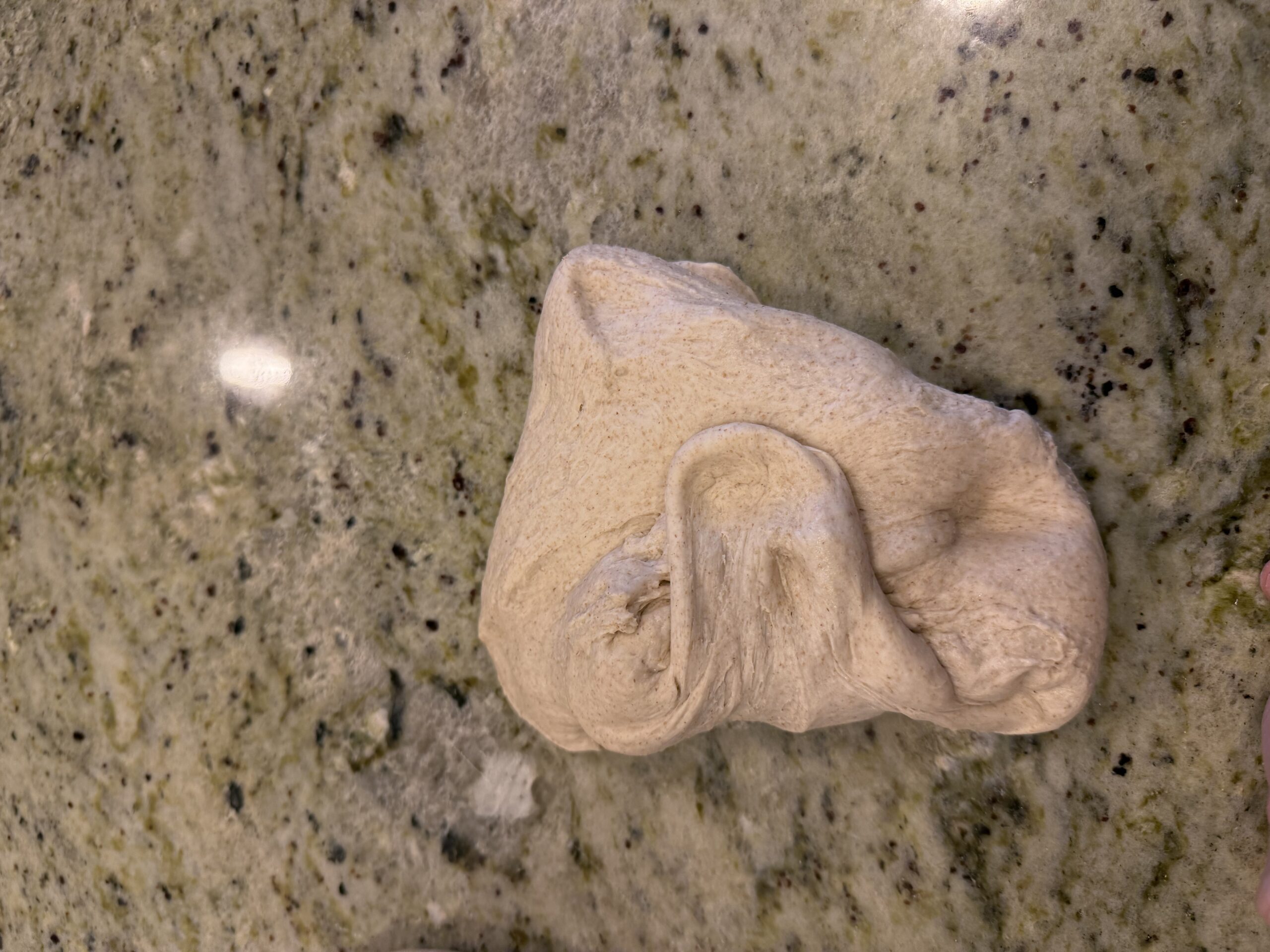 Dough being folded on a granite countertop to build tension
