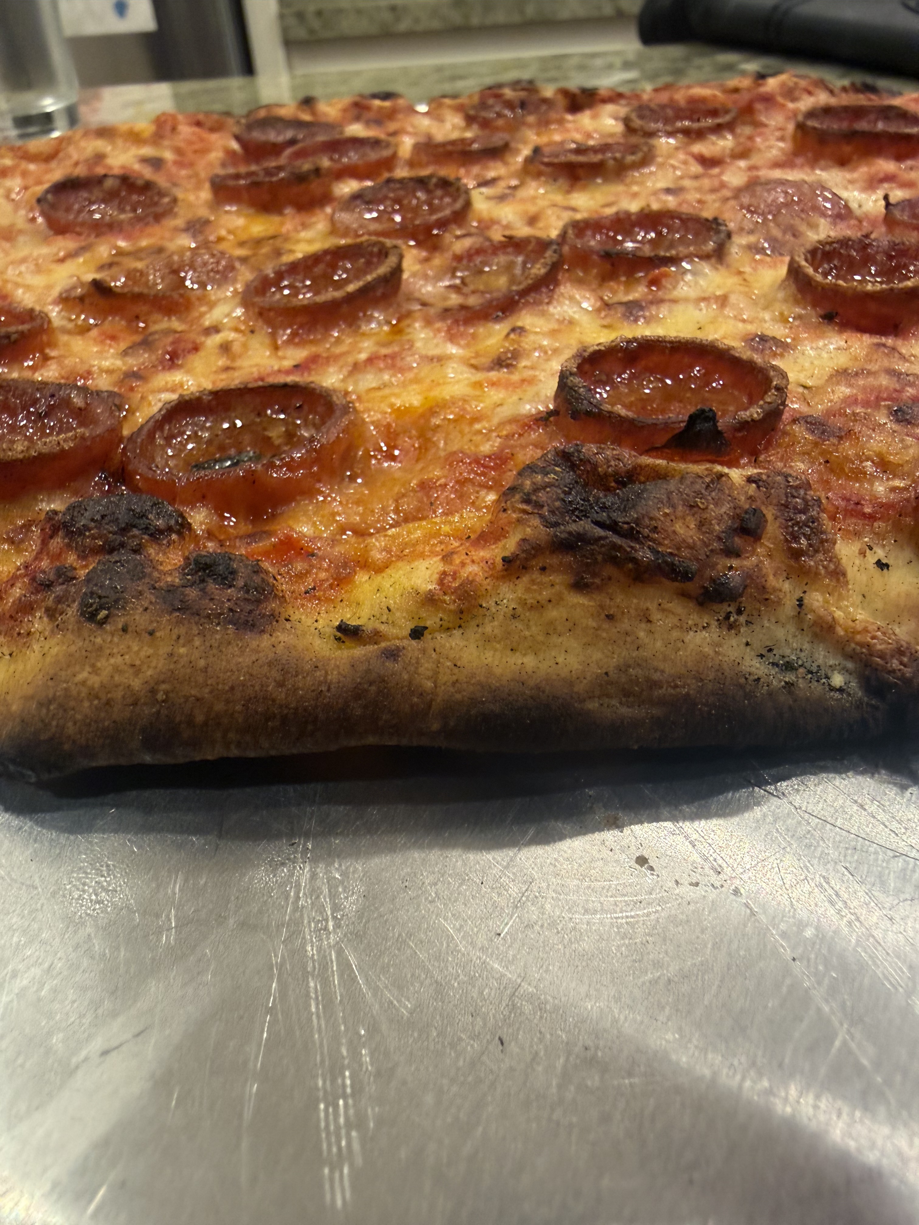Close-up of a Sally's pepperoni apizza showing the puffy charred cornicione and cupped pepperoni