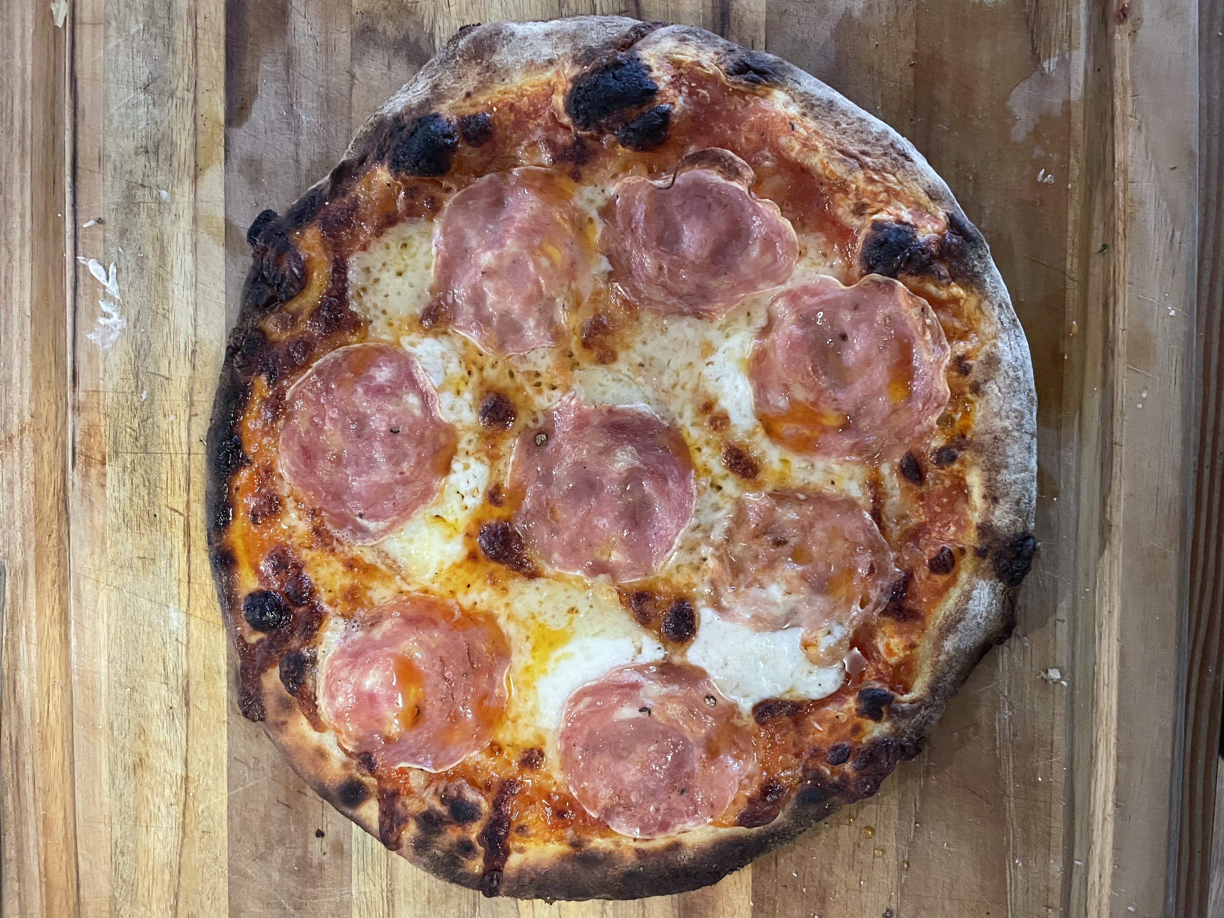 Whole apizza topped with large rounds of salami from Zuppardi's Apizza in West Haven, Connecticut, on a wood board with a charred edge